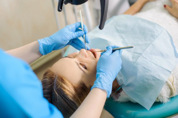 Closeup portrait of young beautiful girl at denist check-up. Doctor holding dental tools wearing gloves. Caries protection. Tooth decay treatment.